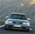 Pixelated static image of a light blue sedan with dark windows and black wheels on a gray road under a muted sky.