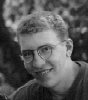 Black-and-white photo of a person with short curly hair and round glasses smiling, cropped into multiple overlapping frames showing progressive zoom on the face.