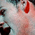 Pixelated close-up of a person's face with light skin tone, red lips, and dark hair, featuring a red teardrop-shaped mark on the right cheek.