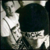 Black-and-white of four showing a person with dark hair wearing a white shirt and patterned overalls, the word "NICK" visible on their chest