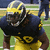 A pixelated image of a football player in a dark blue and yellow uniform with the number 9, positioned on a grass field, with text overlays on a yellow background.