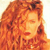 A static pixelated image of a person with long, wavy reddish-brown hair, closed eyes, and a neutral expression against a light background.