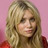 Pixelated close-up of a person with long blonde hair against a pink background, wearing red clothing.