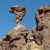 Pixelated image of two rock formations against a blue sky, one resembling a camel's head and neck, the other a larger rock with a dark crevice.