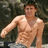A shirtless man with short dark hair stands in front of a blurred background, with green text above his head.