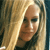 A static pixelated image shows a person with long light brown hair, wearing a dark top, against a blurred background with warm tones.