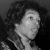 Black-and-white pixelated static image of a person's face and upper shoulders with dark hair against a gradient background, appearing as a low-resolution digital portrait icon.