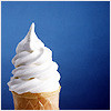 A soft-serve ice cream cone with a tall, swirled white scoop on a light brown waffle cone against a solid blue background.