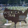 A brown silhouette of the United States map with text reading 'AMERICA IN IRAQ' overlaid, set against a blurred background of a grassy field with white markers.