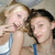 Two people in a close-up pose, one making a peace sign with fingers, wearing sleeveless tops against a light background.