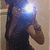 A person in a dark sleeveless top holds a bright light source near their face, with a blurred background and visible arm and shoulder details.