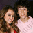 Two people in a close pose on a dark background, with bright pink and gray text displaying 'they r the cutest couple!! *#1 fan!!*' in pixelated font