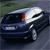 A pixelated dark blue sedan with a white roof is shown in motion on a road, viewed from a low angle with greenery in the background.
