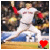 Baseball player in white uniform with red sleeves and number 2, mid-pitching motion on field with blurred stadium background.