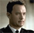 Pixelated close-up of a person in a dark suit and white shirt, facing right with a neutral expression against a light gradient background.