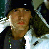 Pixelated static image of a person wearing dark clothing with visible facial features and partial background elements.