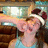 Pixelated image of a person with light skin and brown hair wearing a white headband, holding an object near their face against a blurred background.