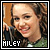 Pixelated square image of a smiling person with curly hair, wearing dark clothing and green fabric, with text 'HILEY' at bottom left.