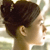 Pixelated profile view of a person with dark hair tied in a bun, light skin, and a neutral expression against a blurred background.