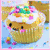 Pixelated cupcake with white frosting, colorful sprinkles, and a smiling face on light blue background; adjacent muffin wears black sunglasses.