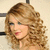 Pixelated close-up of a person with light brown curly hair, closed eyes, and red lips against a beige background.