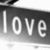 A grayscale image showing the word 'love' in white lowercase letters on a dark background, with a light gradient and faint horizontal lines beneath the text.