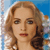 Pixelated close-up of a person with light brown wavy hair, blue background, and visible facial features including eyes, nose, and lips.