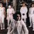 A pixelated static image shows multiple figures in white attire with dark accents against a dark background, appearing to be a low-resolution digital artwork.