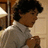 Pixelated image of a person with dark curly hair wearing a light-colored shirt, viewed from the side against a blurred background.