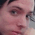 Pixelated close-up of a person's face showing eyes, nose, and mouth with visible skin tones and dark hair strands.