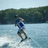 A pixelated image of a person wakeboarding on water with green trees in the background, paired with pixelated text on black and gray