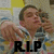 A person in a striped shirt with hand near face, background of yellow and white squares, black text "R.I.P" at bottom.