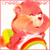 A pink Care Bear with a rainbow belly badge and yellow wing-like prop, smiling with closed eyes against a white background.