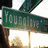 Green street sign reading 'YOUNG' with partial view of another green sign above it, set against a bright background.