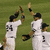 Baseball players in white uniforms with black numbers high-fiving on a grass field.