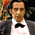Pixelated image of a person in a white dress shirt and black bow tie, with dark hair and a blurred background featuring green and orange tones.