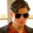 Static 48x48 pixel icon showing a person with short brown hair wearing dark sunglasses and a red shirt under a dark jacket, set against a light background with yellow accents.