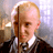 Static pixelated image of a person with light hair wearing dark clothing and white collar, set against blurred background with warm and cool tones.