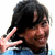 A person with dark hair and a blue shirt makes a peace sign, smiling while turning their head slightly left to right across frames.