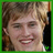 A pixelated close-up of a person with light brown hair and fair skin smiling, framed by green borders with small symbols at the bottom corners.