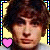 Pixelated static icon featuring a person with dark curly hair against a yellow background, bordered by blue and cyan pixelated frame elements with a pink heart symbol in the bottom-left corner.