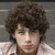 A person with curly brown hair wearing a light-colored checkered shirt appears in three showing subtle head movement