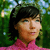 Pixelated portrait of a person with dark hair wearing a pink top against a green and blue background.
