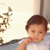 Pixelated image of a child with short brown hair wearing a white shirt, positioned against a light background with blurred vertical elements.