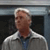 Pixelated image of a person with light hair wearing a light jacket over a dark shirt and blue tie, set against a dark background with a light horizontal band.