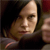 Pixelated close-up of a person with light skin tone, dark hair, and a dark top, set against a dark background with brown and red tones.