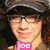A person with curly hair wearing a dark cap and glasses, smiling in a of six with pink text overlays