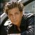Static pixelated image of a person with light brown hair wearing dark clothing, visible against a blurred background.