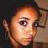 Pixelated close-up of a person with light brown hair, dark eyes, and a neutral expression against a dark background with a brown object on the right.