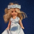 A blonde woman in a white dress with blue accents and a headband, shown across against a dark background